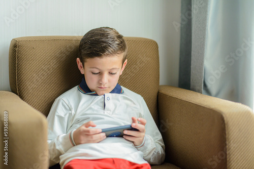Child sitting in an armchair playing with a smartphone. photo