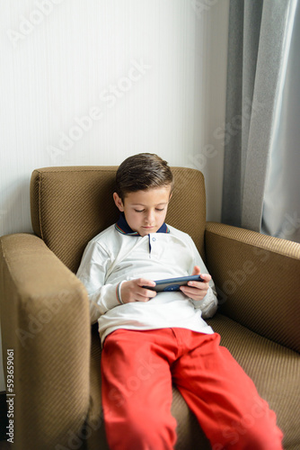 Child sitting in an armchair playing with a smartphone.