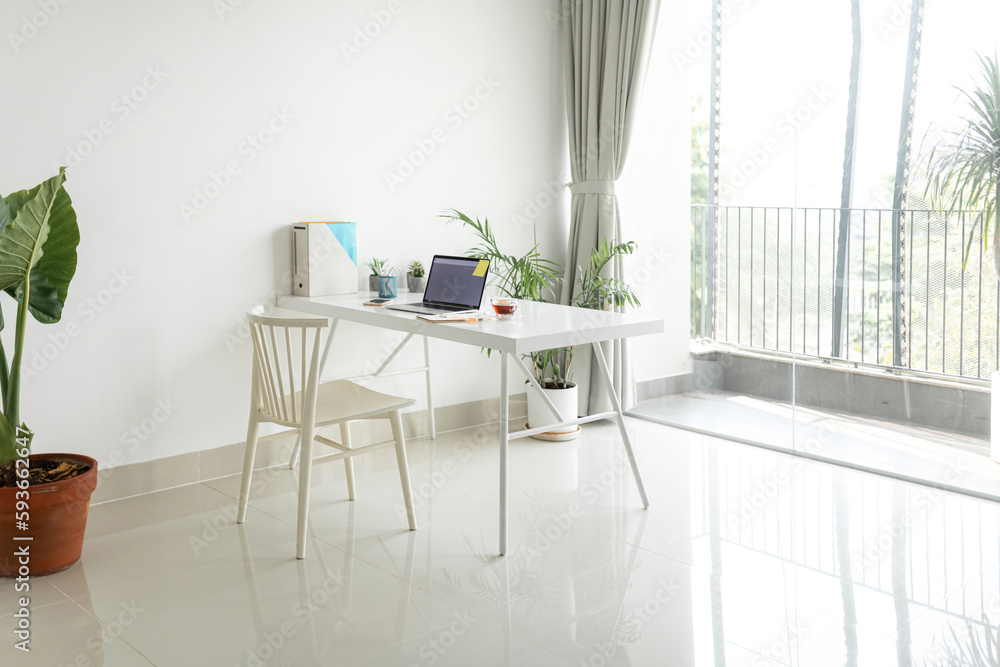© Marc Tran/Stocksy - Front view laptop computer, flower pot and coffee cup on white