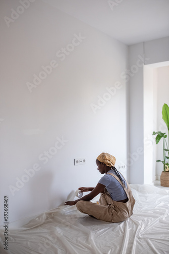 Black woman covering baseboard with painter tape