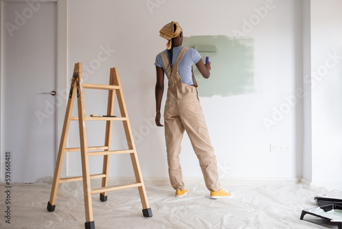 Black woman painting wall near door