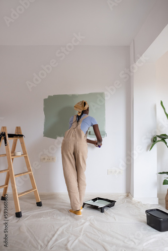 Black woman in overalls painting wall