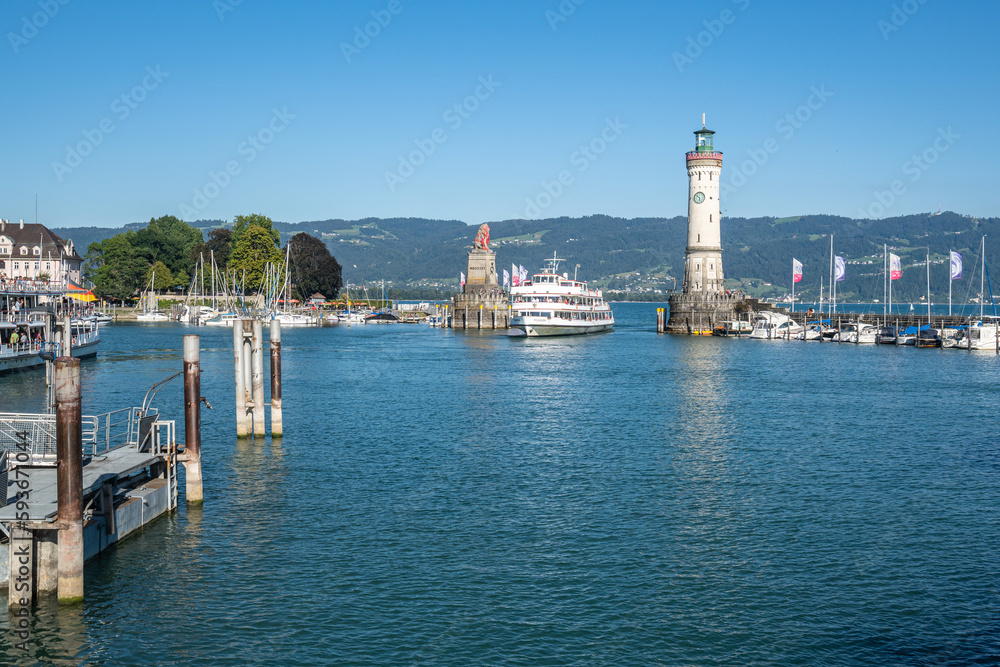 A ferry entering in Lindau port passing between the lighthouse and iconic Bavarian Lion sculpture, Bavaria, Germany