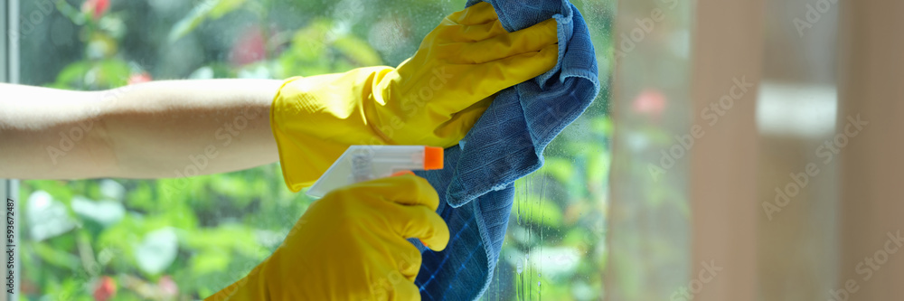 Female hands in gloves cleaning window using detergent and rags Female hands in gloves cleaning window using detergent and rags