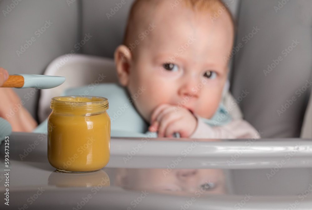 A small child 5-6 months old looks at a jar of vegetable and fruit puree. Feeding babies, caloric content of food. Copy space for text A small child 5-6 months old looks at a jar of vegetable and fruit puree. Feeding babies, caloric content of food. Copy space for text