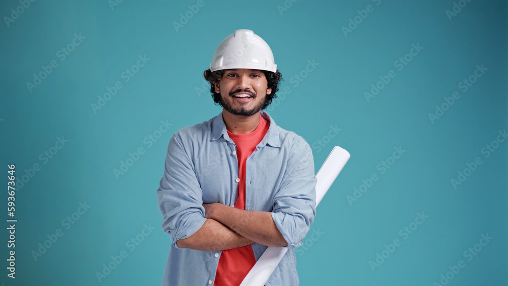 People and work concept. Positive indian or arabic construction architect male worker wears hardhat holds blueprint smiles gladfully to the camera isolated over blue background People and work concept. Positive indian or arabic construction architect male worker wears hardhat holds blueprint smiles gladfully to the camera isolated over blue background