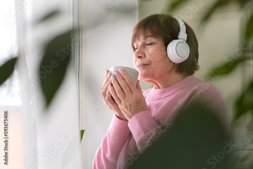 portrait of an elderly woman lost in her thoughts while standing by a window, evoking the challenges of aging and the universal feeling of solitude that comes with it.