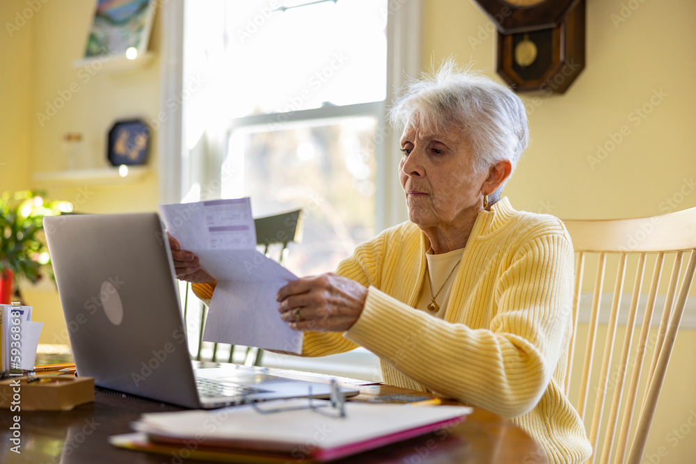 Senior Citizen at Home reading bills looking at laptop yellow room Senior Citizen at Home reading bills looking at laptop yellow room