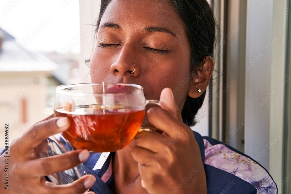 Relaxed and Cozy: Young Indian woman enjoys hot tea on her windowsill.