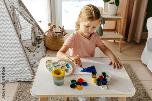 Little girl painting with gouache at table