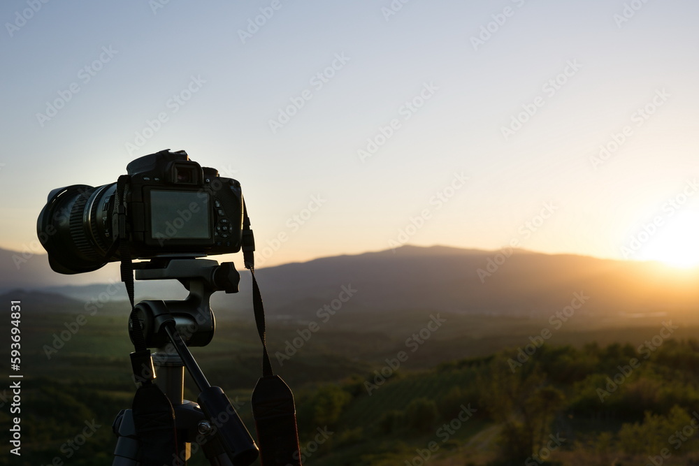 Tripod camera against landscape at sunrise