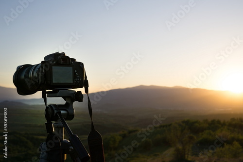 Tripod camera against landscape at sunrise