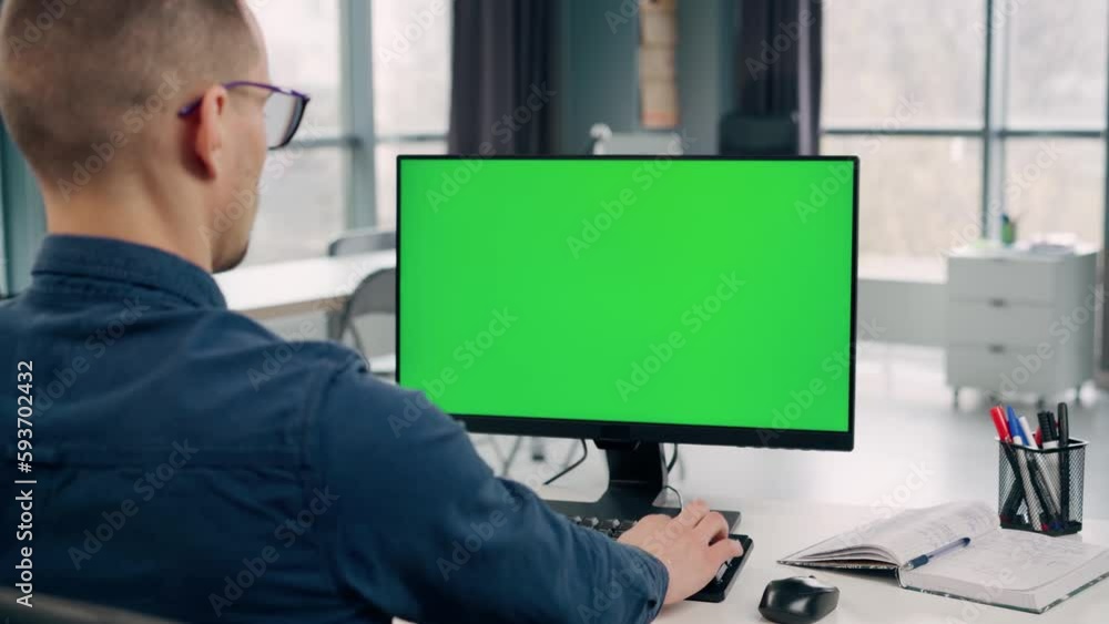 Young Man Working At Computer With Green Mock Up Screen in Office. Man Typing on Keyboard and Looking at PC Display Young Man Working At Computer With Green Mock Up Screen in Office. Man Typing on Keyboard and Looking at PC Display