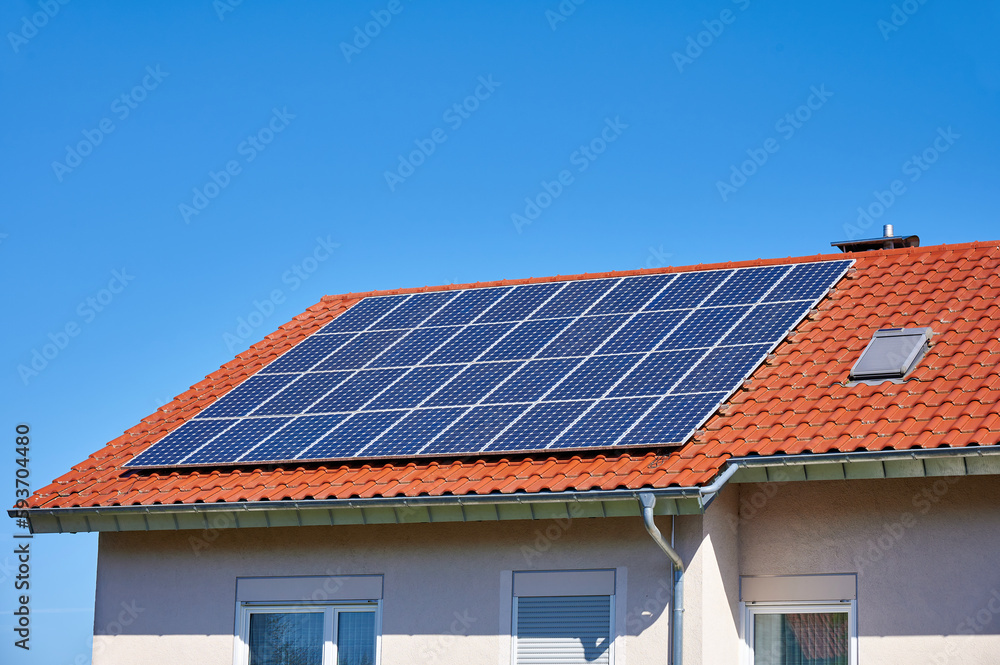 Fototapeta premium Solarzellen auf rotem Hausdach vor blauem Himmel
