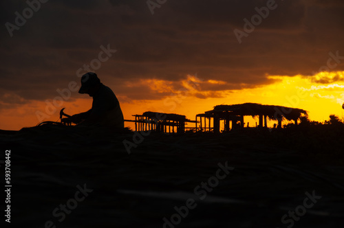 A silhouette of a man fixing a beach hut by the ocean at dawn