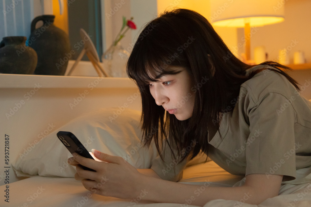 Focused Asian woman browsing mobile in bed Focused Asian woman browsing mobile in bed