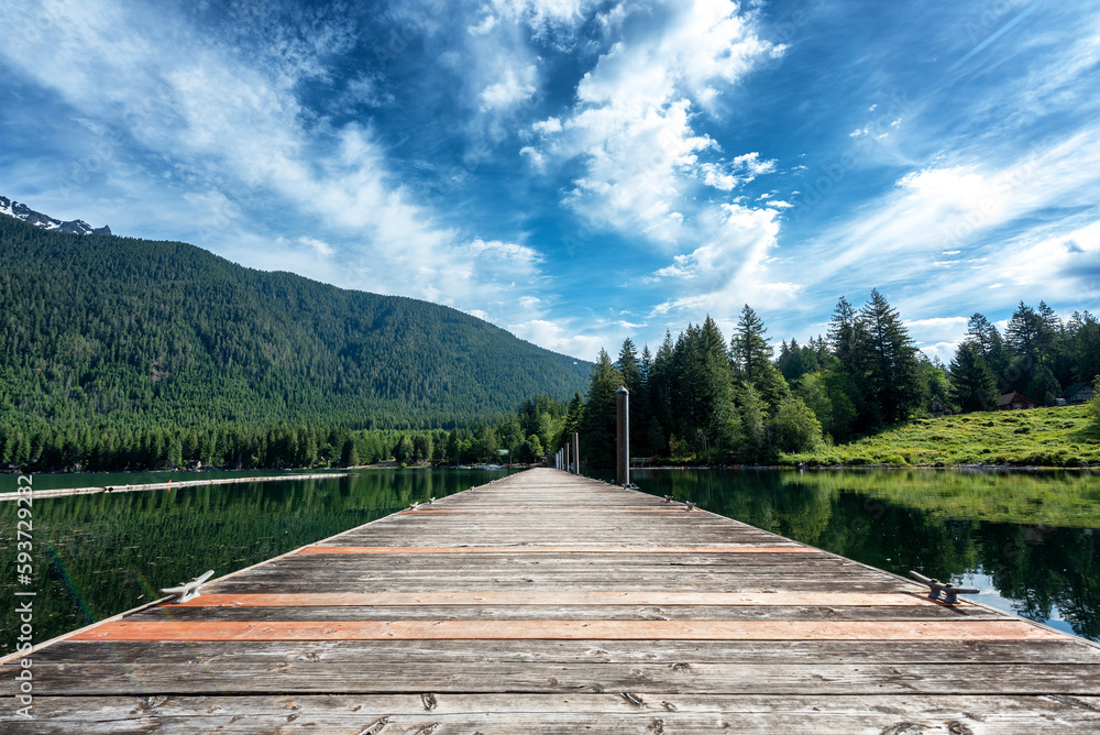 Idyllic view of a wooden pier in the lake with lush forested mountain in the background under wispy clouds