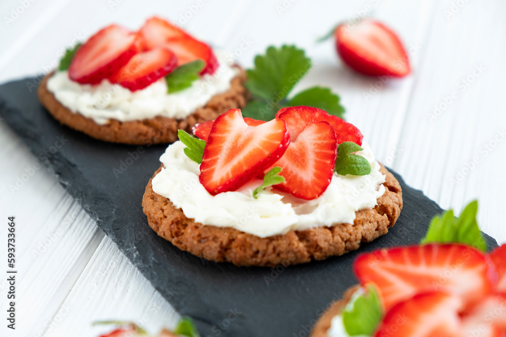 Strawberry tart with oat biscuit and whipped cream on black slate board. Recipe of simple berry cake for breakfast or holiday. Summer light dessert.