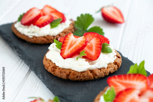Strawberry tart with oat biscuit and whipped cream on black slate board. Recipe of simple berry cake for breakfast or holiday. Summer light dessert.