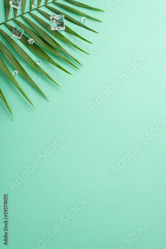 Top view of summertime floral vertical flat lay with green palm leaves with ice cubes on pastel teal background with an empty space for text or advert