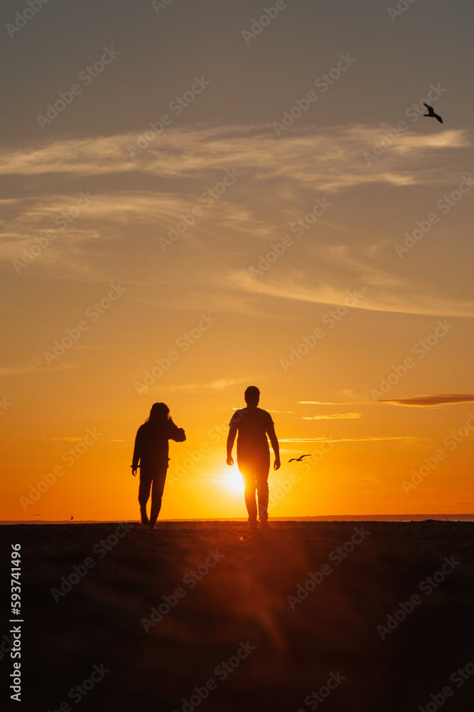 silhouette of a couple at sunset, woman and man walking along seashore in rays of sunset sunlight. walk and hug. place for text, romantic relationships, freedom and carelessness silhouette of a couple at sunset, woman and man walking along seashore in rays of sunset sunlight. walk and hug. place for text, romantic relationships, freedom and carelessness