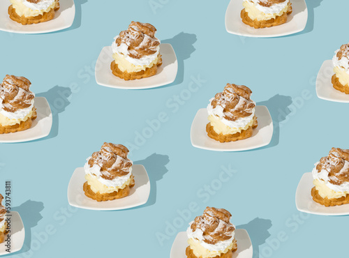 Trendy seamless pattern made with cream puffs on blue background. Minimal food concept. Cream puffs filled with pastry cream and sprinkled with powdered sugar.
