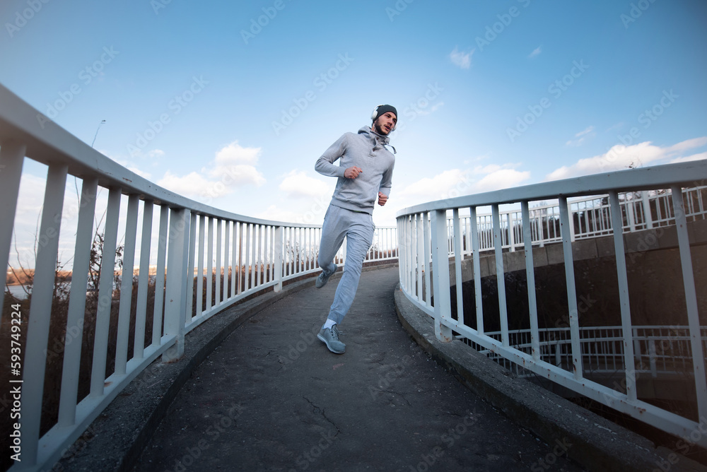 Young powerful male athlete with headphones doing his daily running routine over the bridge