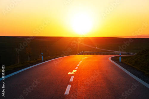 The paved road winds through farmland until sunset.