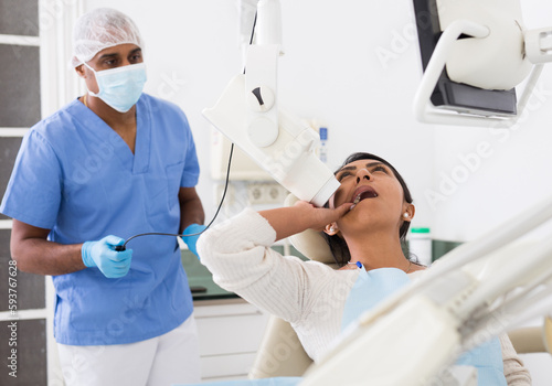 Dentist taking teeth radiography to hispanic female patient lying in chair in dentistry office