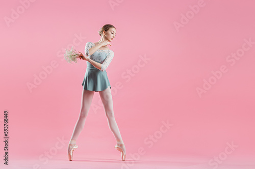 elegant young ballerina in pointe shoes dancing on a delicate pink background