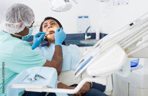 Latin american female patient sitting with open mouth in chair in dental office during checkup at dentist