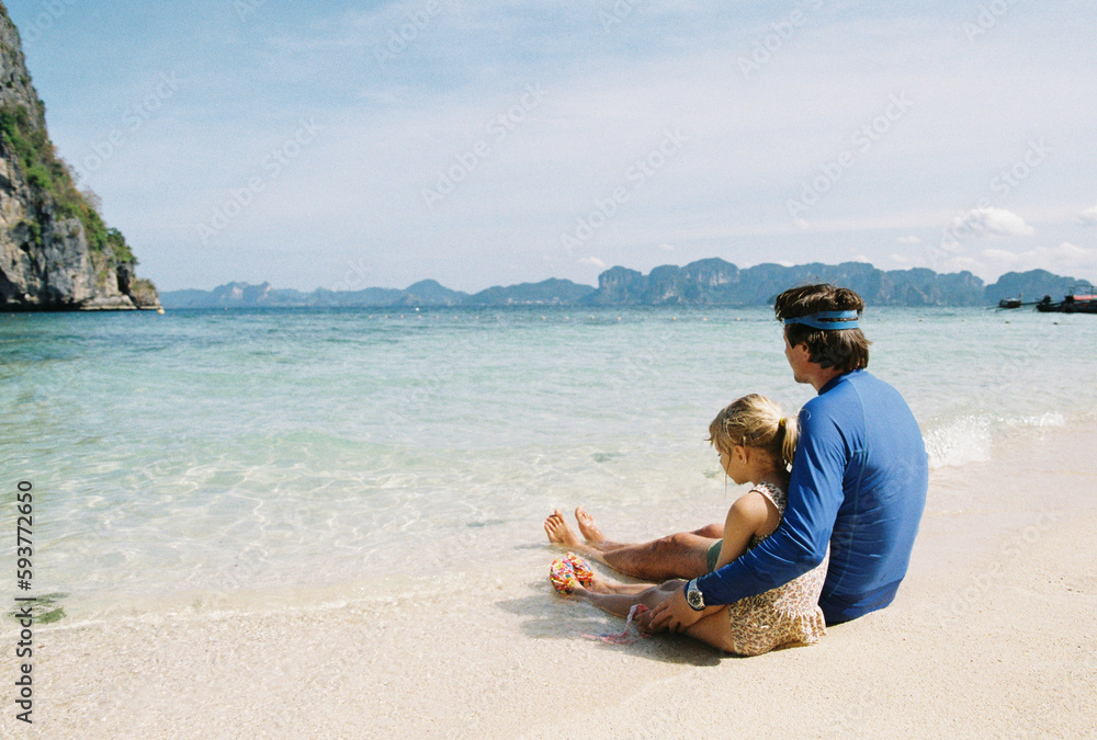 Father and daughter resting on the beach with feet in the water