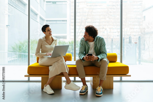 Coworkers discussing project sitting on yellow sofa in a workspace