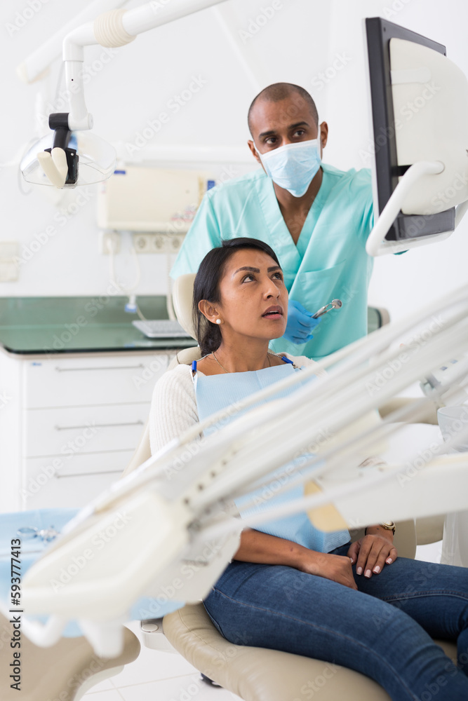 Latin american dentist talking to woman during dental checkup