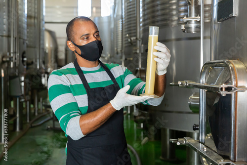 Winemaker in mask checking wine at fermentation department of winery, winemaking process