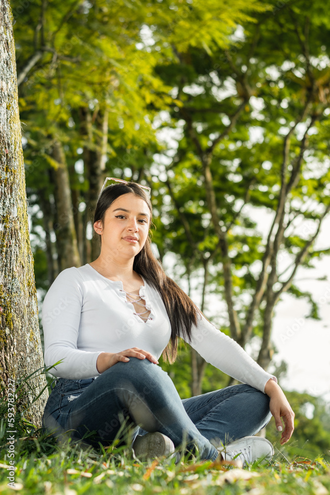 vertical portrait of beautiful latin woman sitting cross-legged on the grass in an open-air park vertical portrait of beautiful latin woman sitting cross-legged on the grass in an open-air park