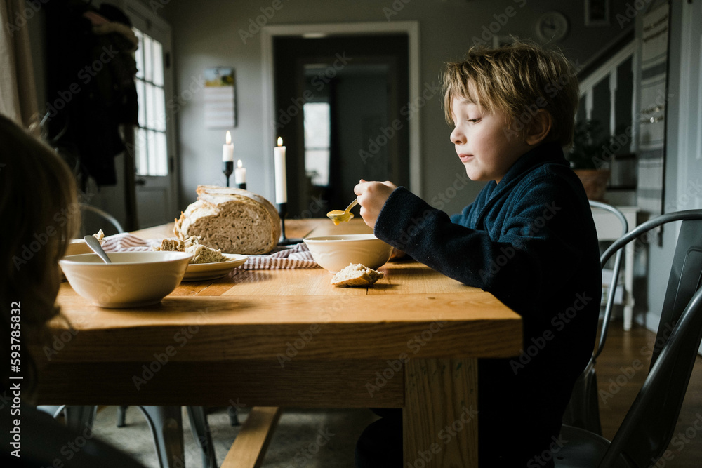 Two children sitting at dining table eating butternut squash soup Two children sitting at dining table eating butternut squash soup