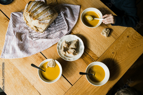 little boy sitting at wooden dining table eating soup 
