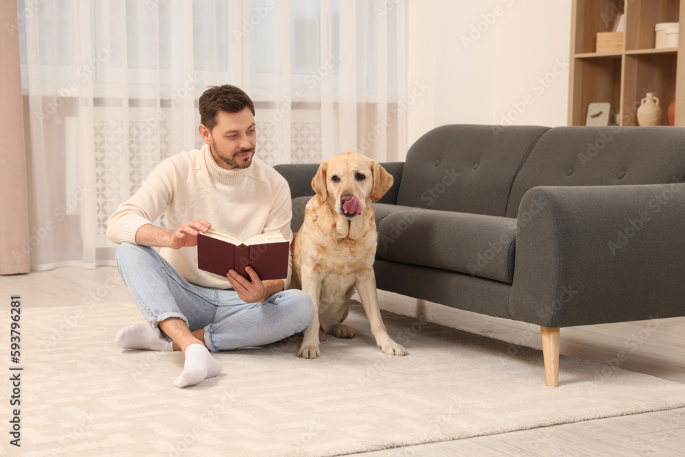 Man reading book on floor near his cute Labrador Retriever at home Man reading book on floor near his cute Labrador Retriever at home