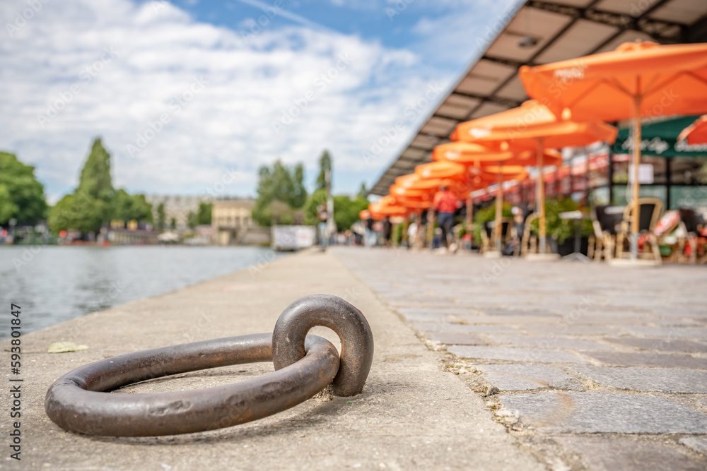 Naklejka premium In Paris, in the Canal Saint Martin area, close up focus on a boat moor along the canal, with a colorful cafe blurred beyond.