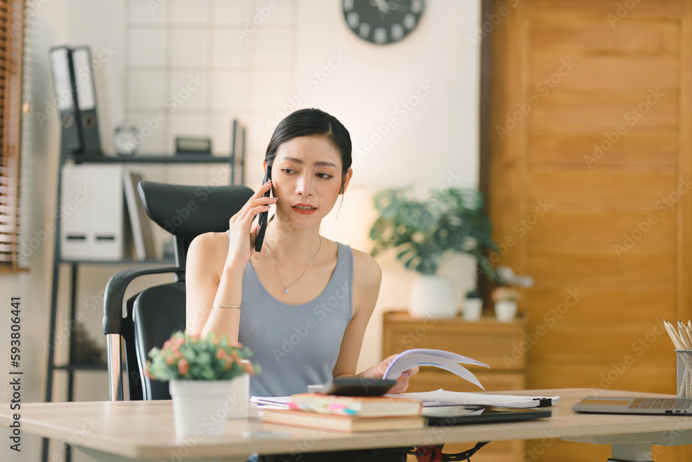 The millennial Asian young businesswoman adviser is analyzing and discussing the financial report situation on cellphone in her home office, financial, accounting, and investment advisor concepts.