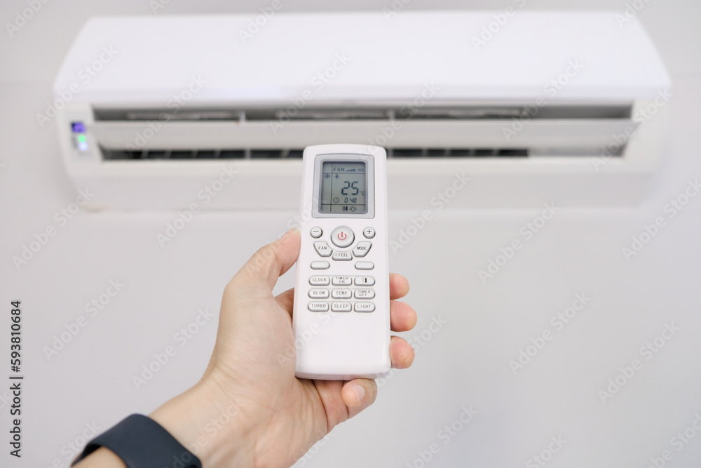 Man's hand using remote control open The air conditioner is cooled to 25 degrees Celsius in his bedroom. Health concepts and energy savings