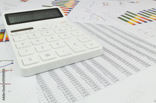 Wide angle image of white calculator on documents with charts and numbers.