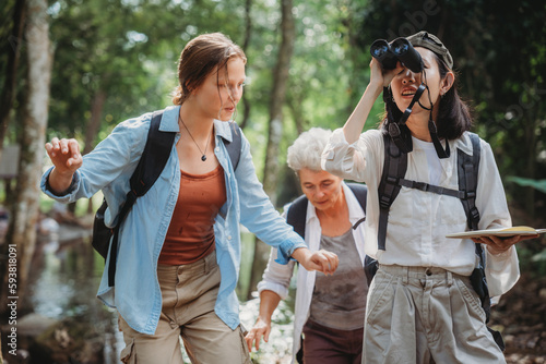 woman family walking in the forest to watching a bird in nature, using binocular for birding by looking on a tree, adventure travel activity in outdoor trekking lifestyle, searching wildlife in jungle photo