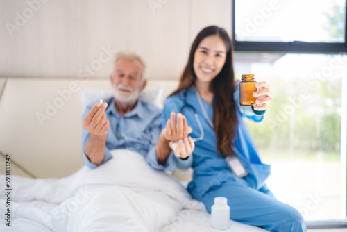 Smiling young nurse in hospital and health care center giving routine medications to happy and cheerful senior patient lying and sitting on bed while having a fun conversation © chokniti