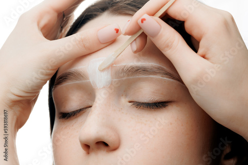 Correction Eyebrow hair waxing. Master combs eyebrows of woman in beauty salon