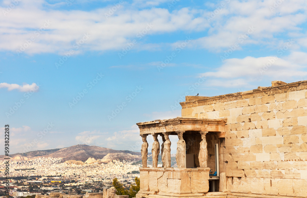 Greece. Acropolis of Athens. View of famous porch with six caryatid statues supporting architrave of Erechtheion against backdrop of Athens city and blue sky. Summer travel and excursions concept