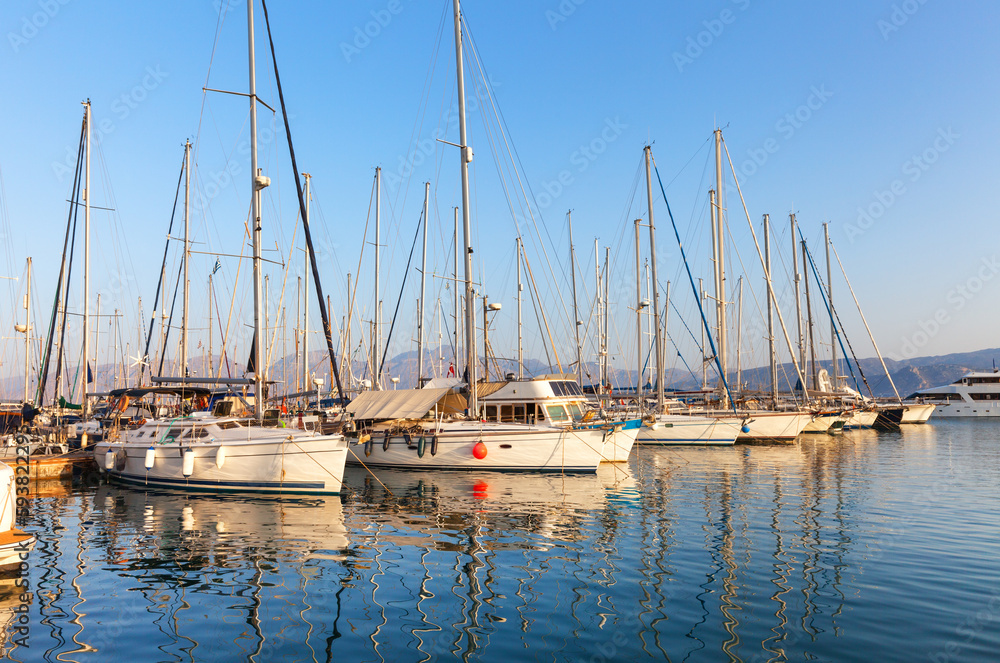 Greece. Crete Island. Beautiful seascape with yachts in Agios Nikolaos Marina in sunset. The masts of yachts are reflected in the blue water of the Mirabello Bay. Summer travel and seaside holidays