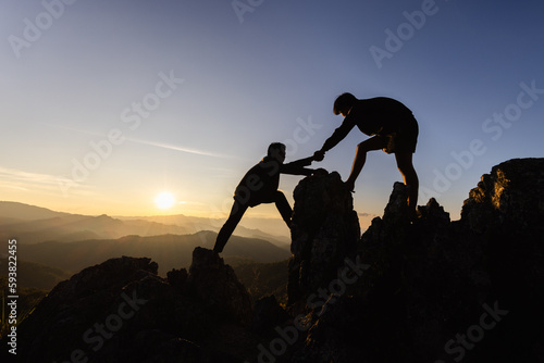Silhouette Teamwork, Male hikers climbing up mountain cliff and one of them giving helping hand. People helping and, team work concept.