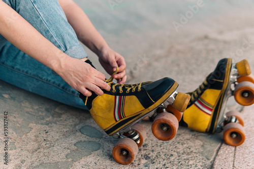 vista desde cerca de patines de cuatro ruedas de colores, con manos de mujer acomodando cordones. photo